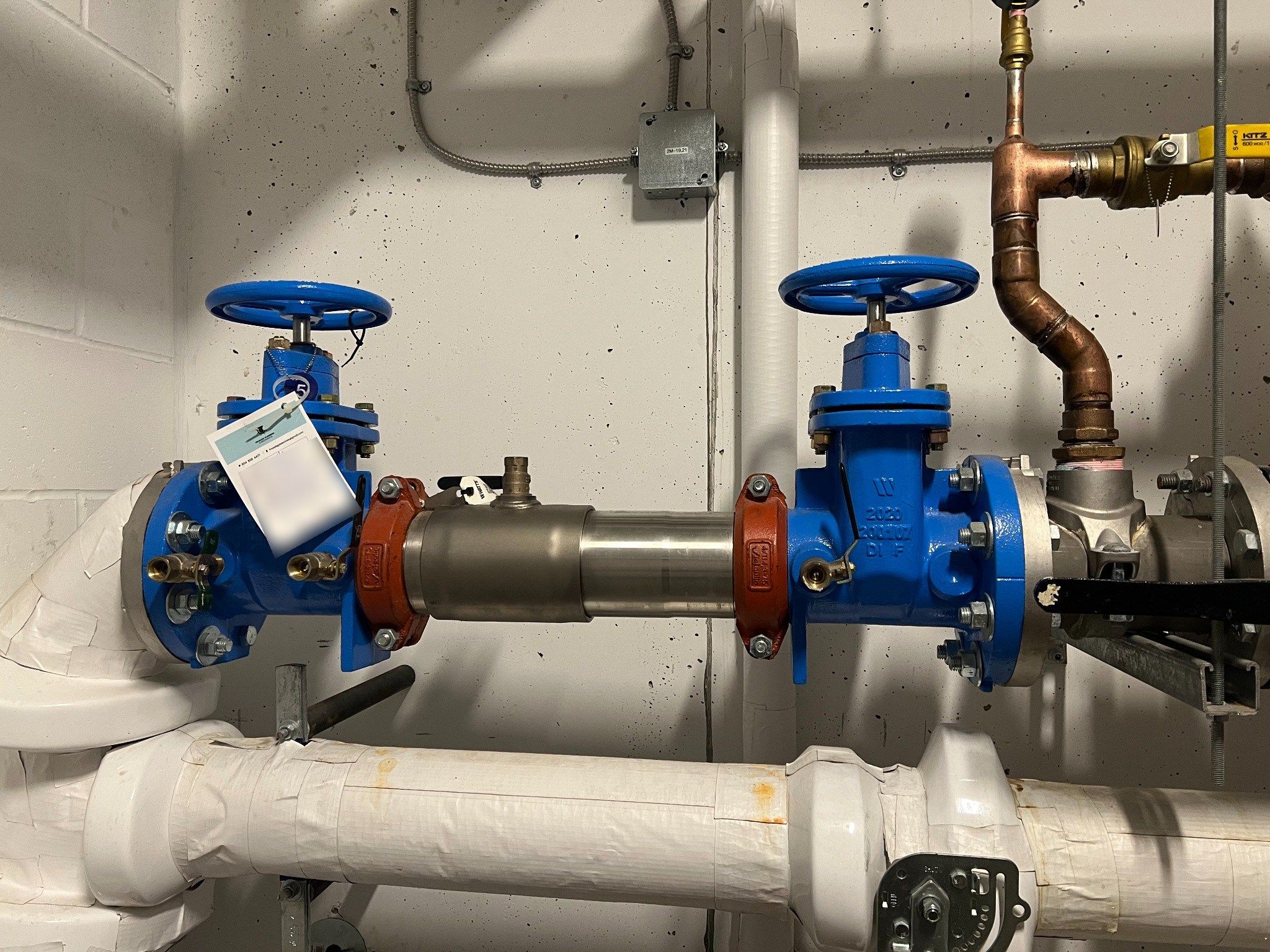 4-inch double-check valve assembly with blue handwheels and a Prosafe test tag in a building mechanical room