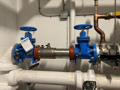 4-inch double-check valve assembly with blue handwheels and a Prosafe test tag in a building mechanical room